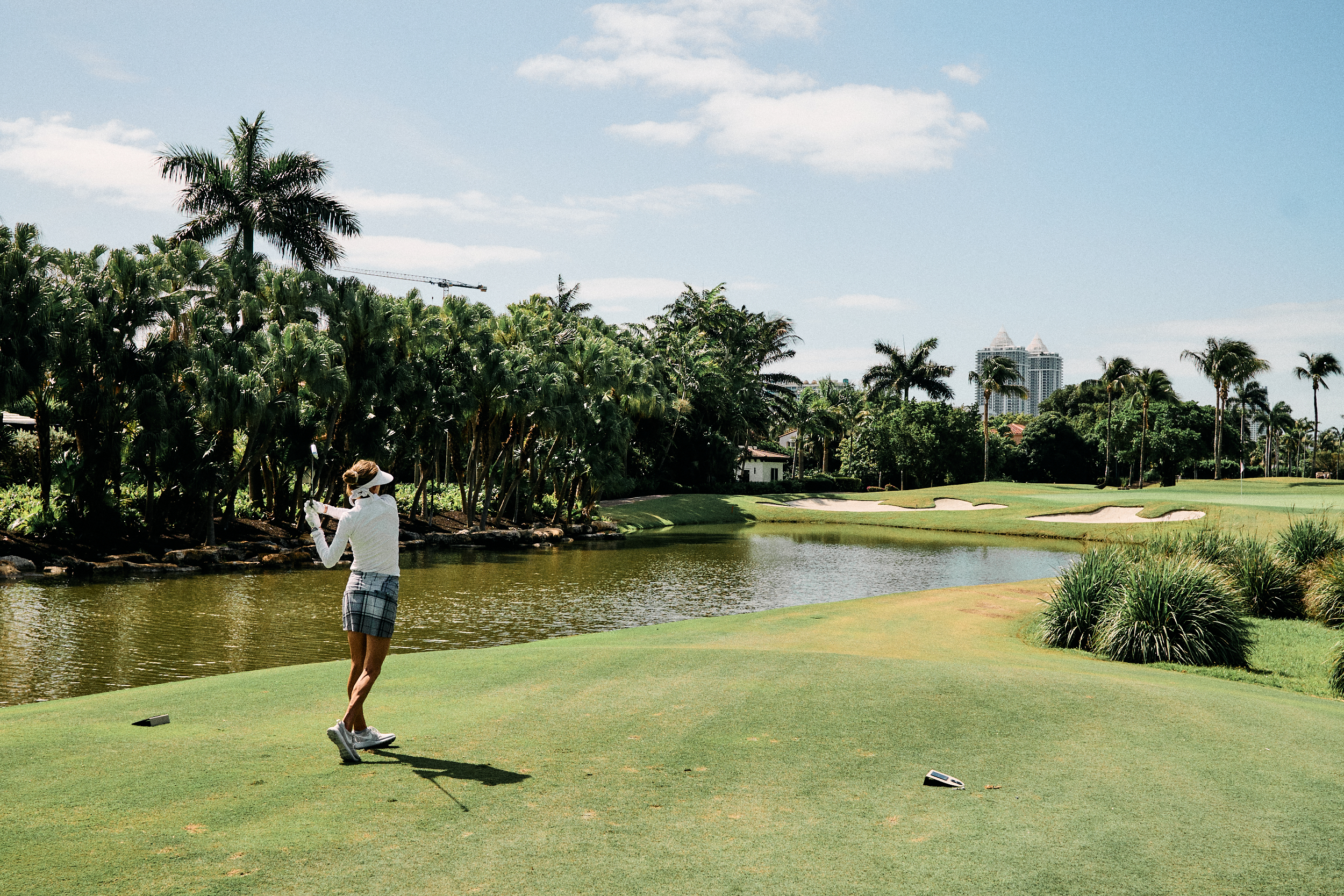 woman golfer mid swing during a relaxed lifestyle photography session hitting a shot on to a par 3 golf green over water.f